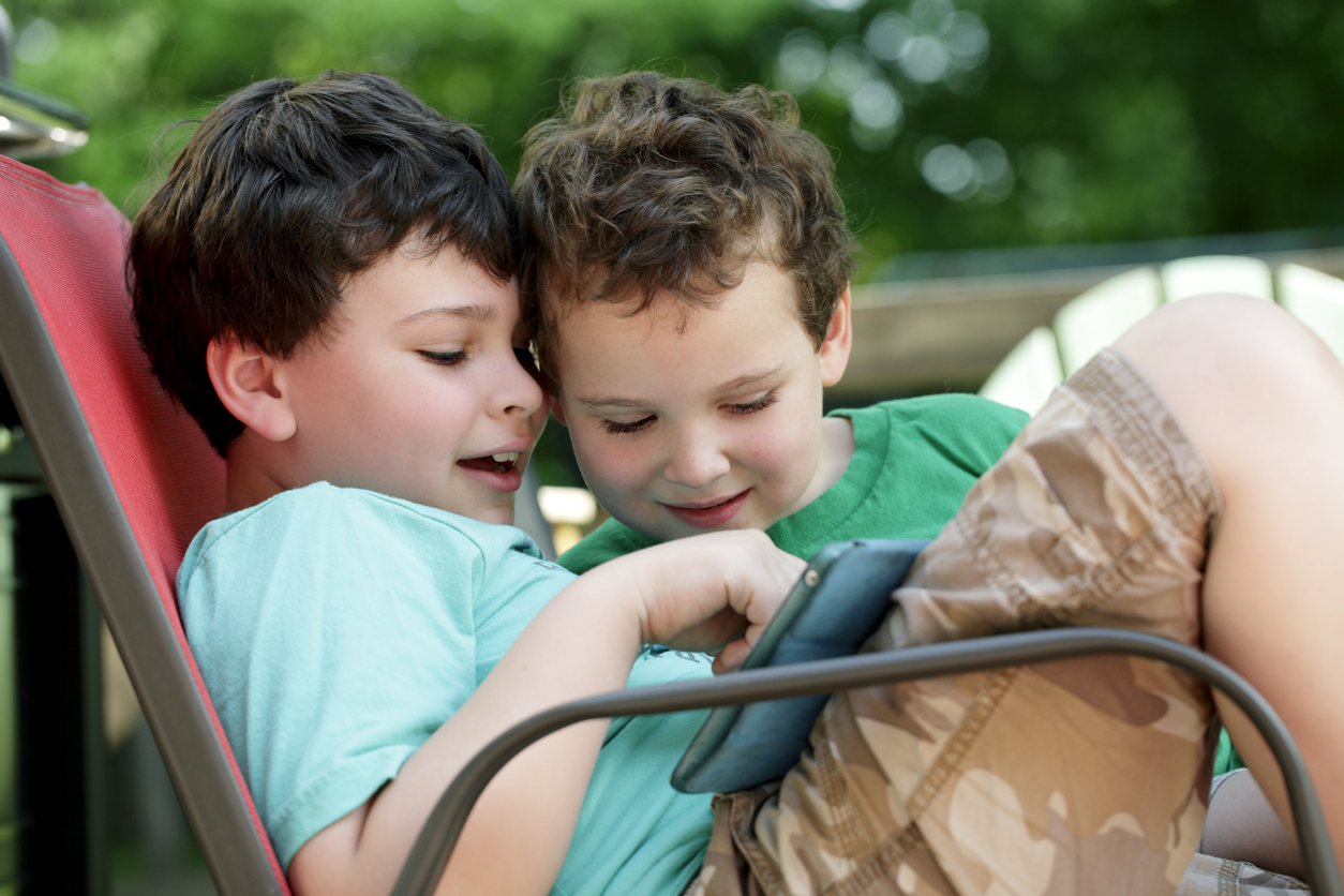 Kids with autism using a tablet while sitting outdoors.