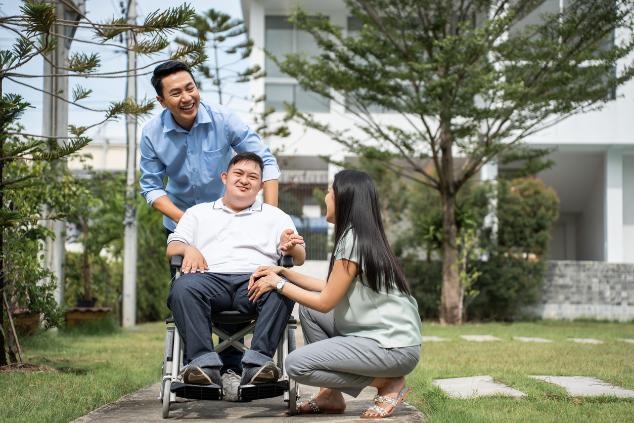 Father and mother taking care of a young man on a wheelchair outside their home.